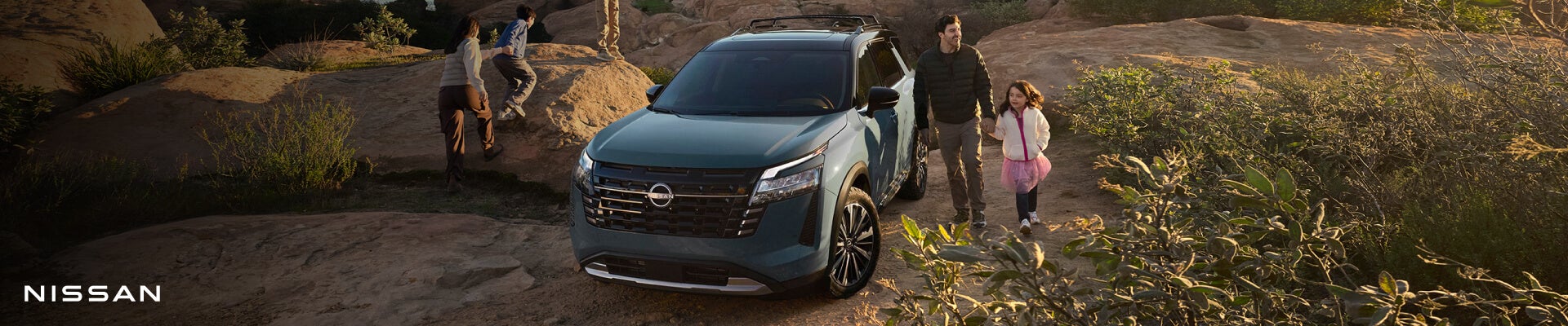 Front-three-quarter view of a Nissan Pathfinder Platinum in Baltic Teal Pearl parked on a dirt path in a rocky desert landscape.