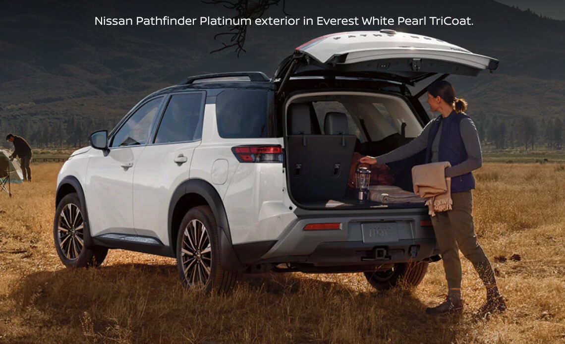 Rear-three-quarter view of a Nissan Pathfinder Platinum in Everest White Pearl TriCoat with an open liftgate at a grassy campsite.