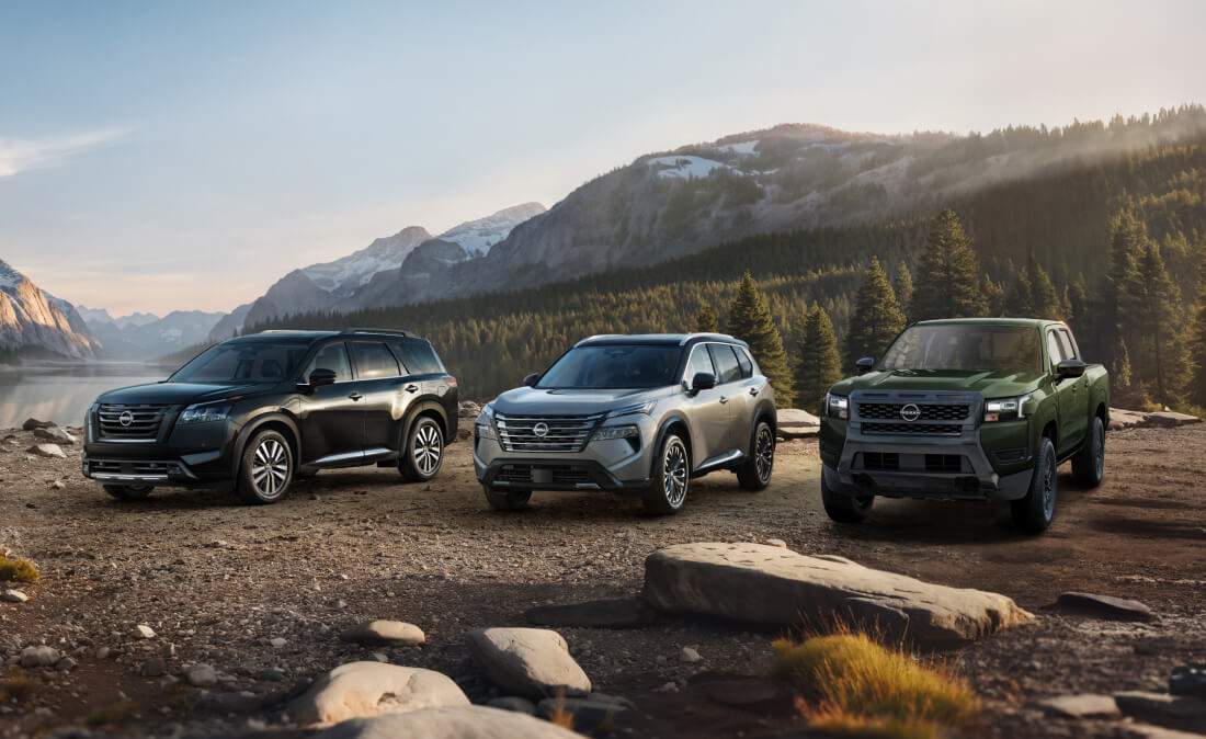 Front three-quarter view of black Pathfinder, silver Rogue, and green Frontier parked near a lake with mountains.